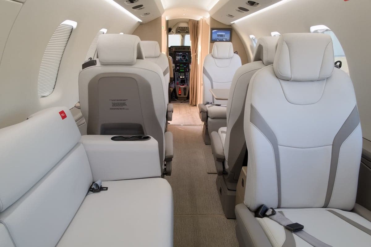 View of the aircraft's interior cabin with white leather seats and a small monitor.