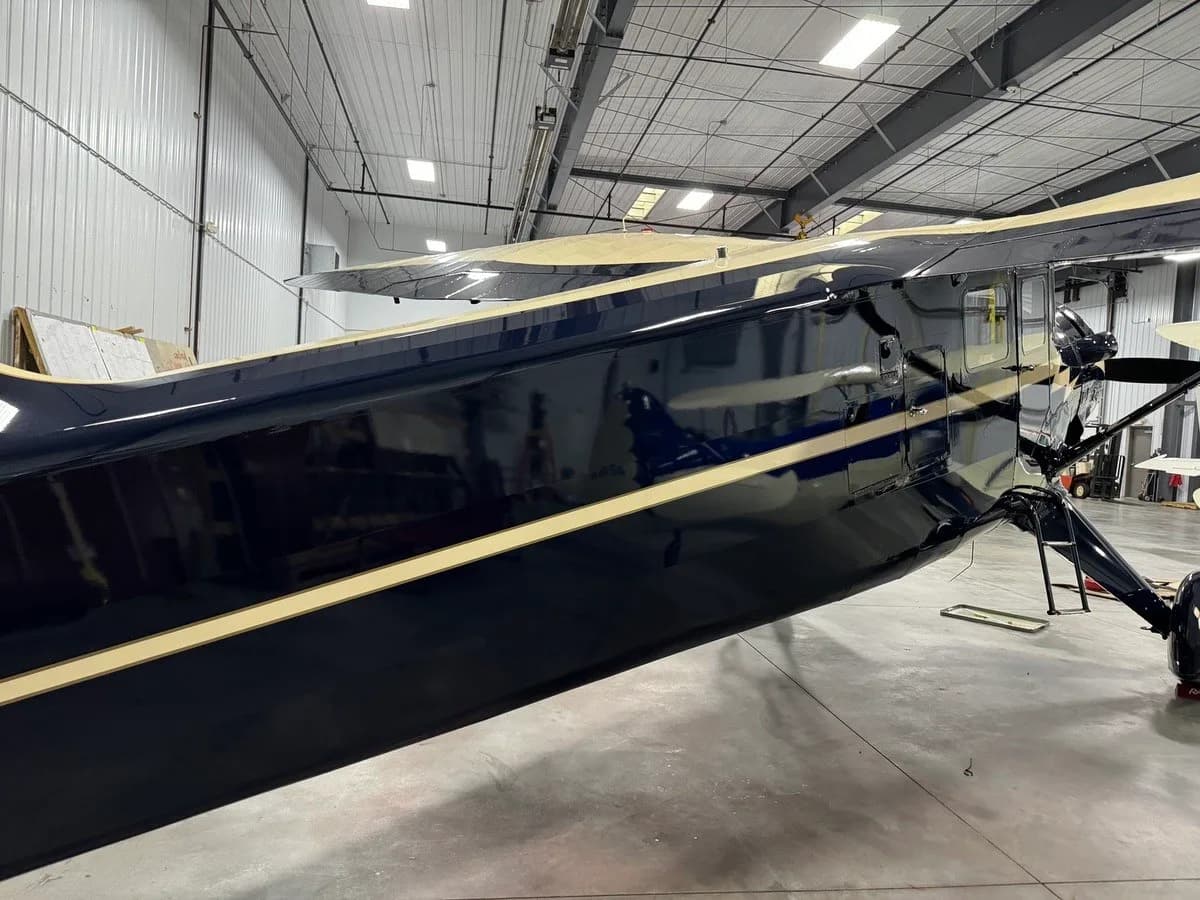 A close-up side view of the shiny dark blue and cream fuselage of a vintage aircraft in a hangar.