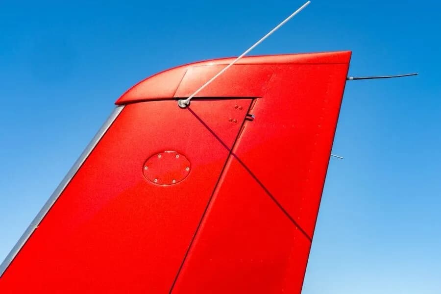 A close-up view of the red vertical stabilizer and antenna of the aircraft against a blue sky.