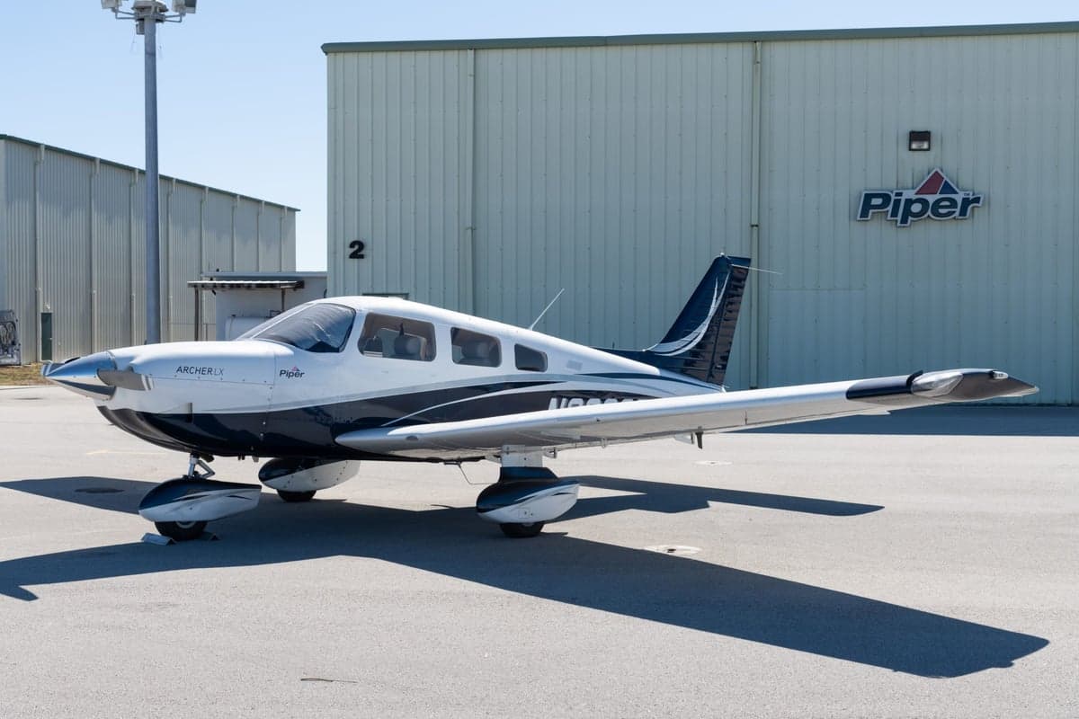 Side view of the Piper Archer LX N603CE in front of a hangar with the Piper logo.