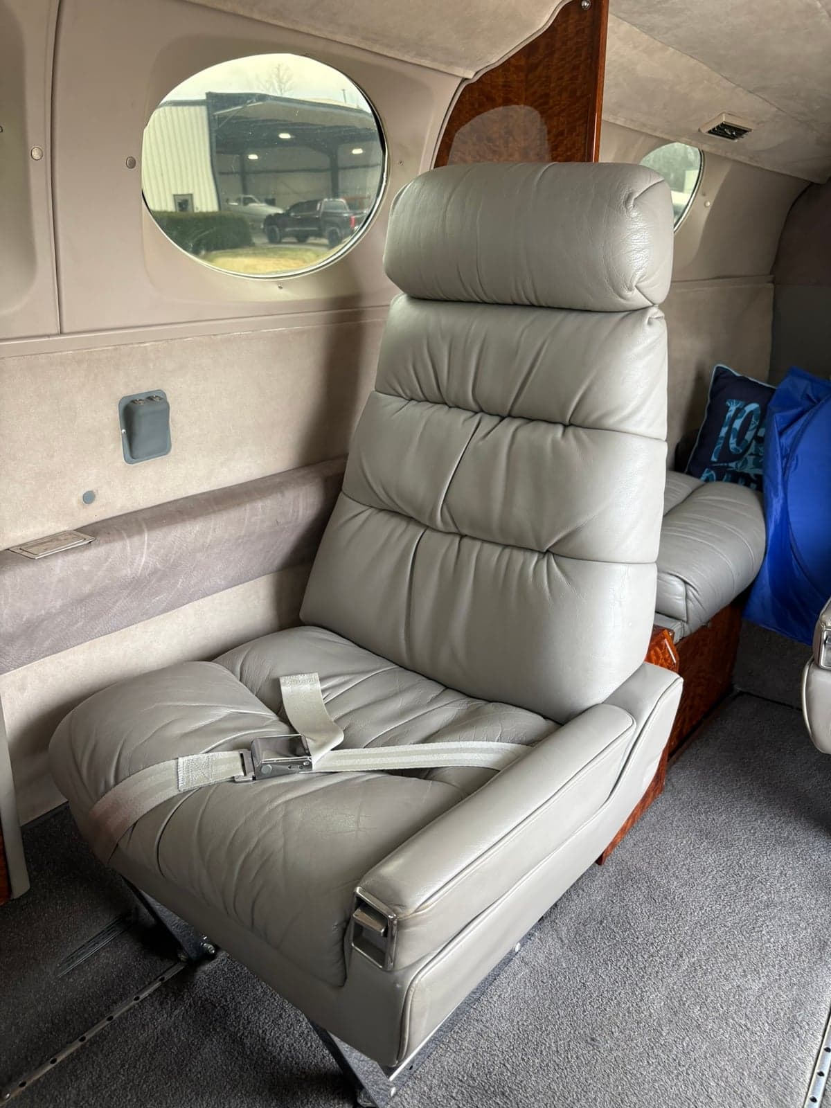 A single grey leather cabin seat with a seatbelt in the aircraft interior, showing a window view outside.