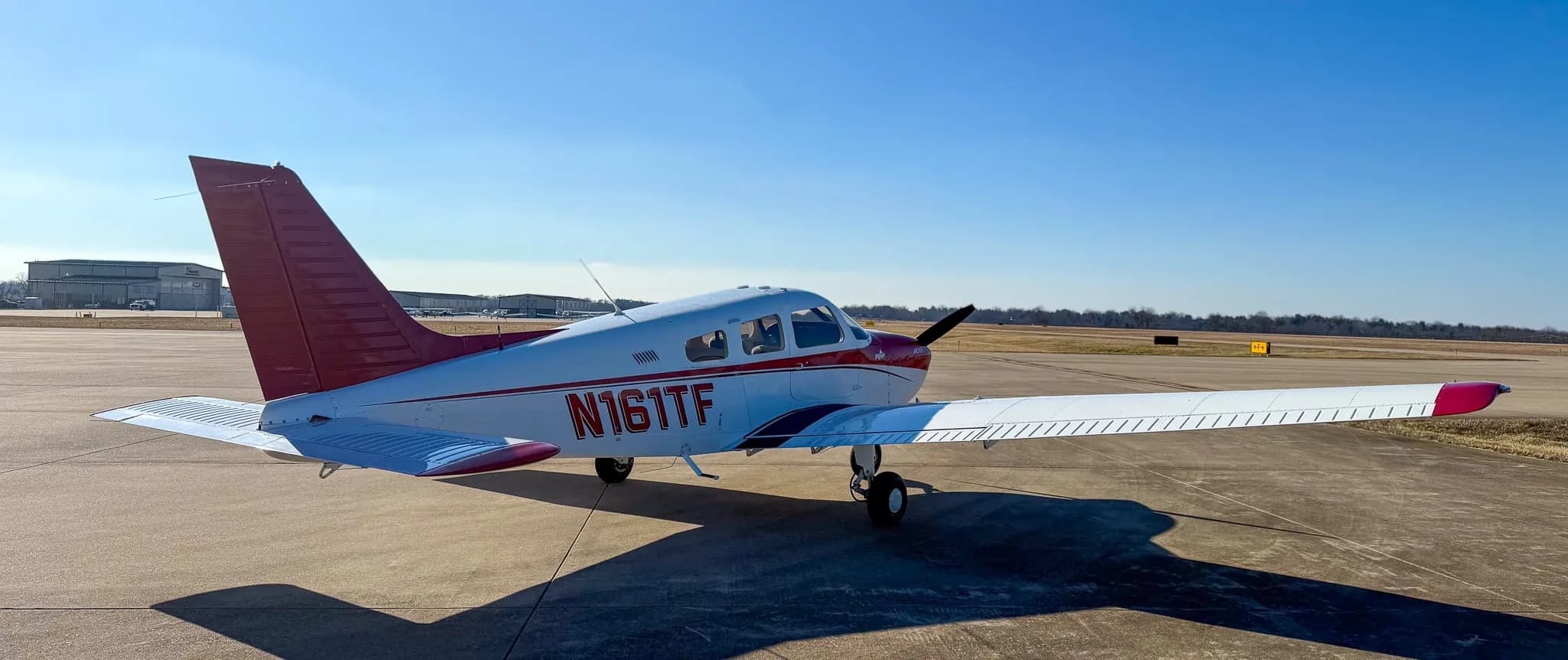 A rear-right view of a red and white Piper Archer TX aircraft, tail number N161TF, parked on an asphalt tarmac.