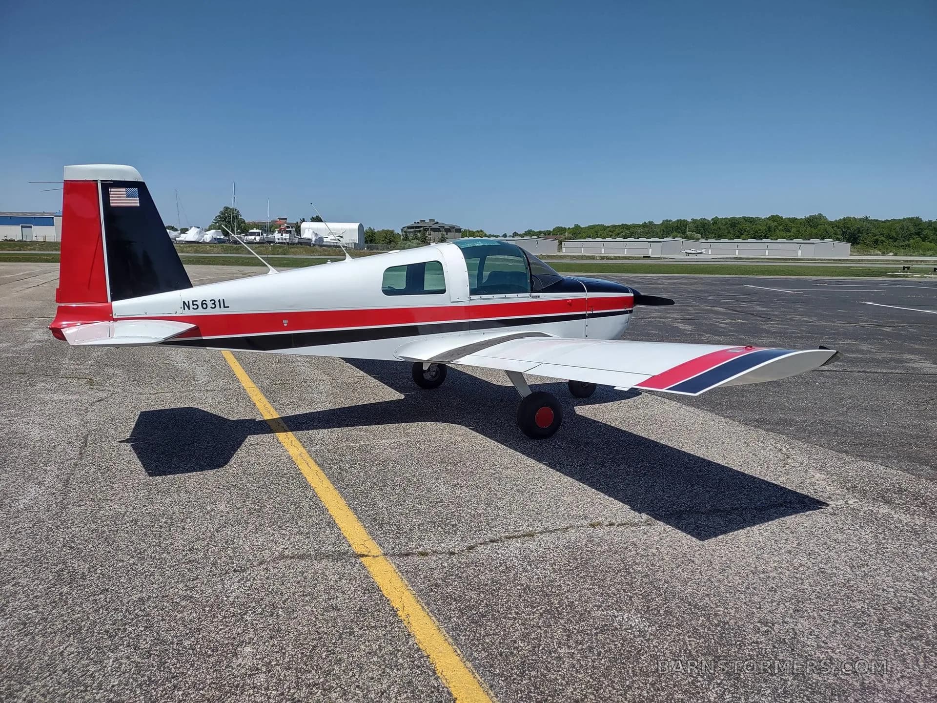 A side view of a white, red, and black single-engine aircraft with tail number N5631L parked on an airfield.