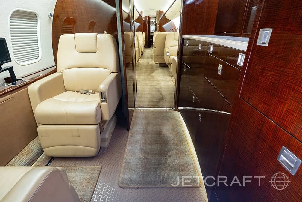 View of a luxurious aircraft cabin with beige leather seats and dark wood paneling.