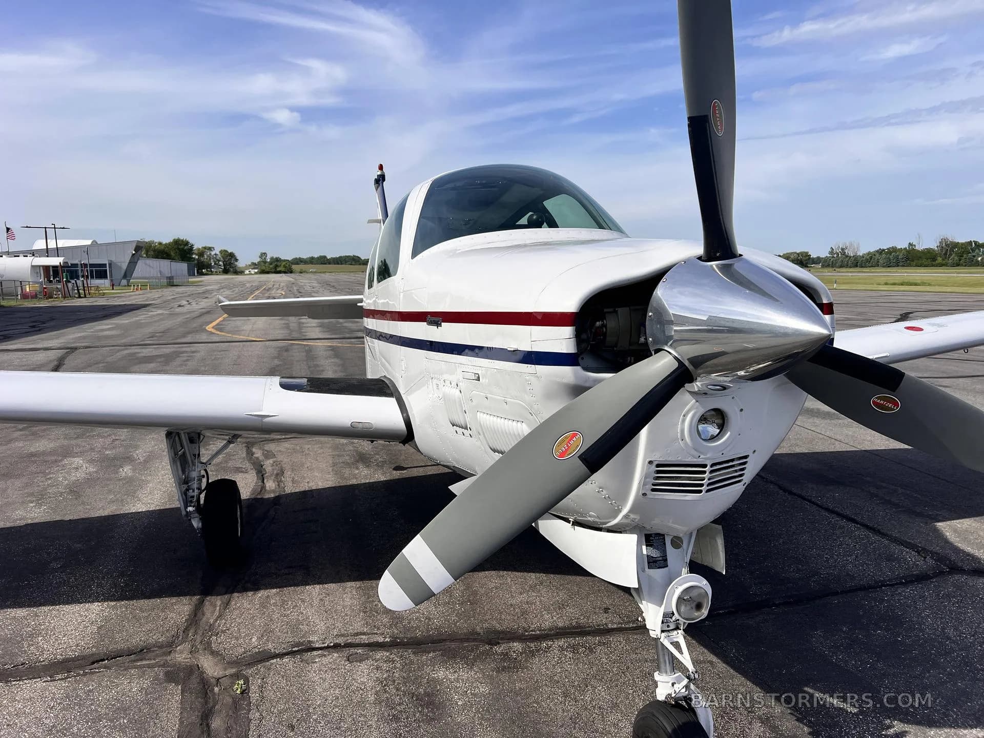 A close-up front view of a white single-engine propeller aircraft with red and blue stripes on a tarmac.