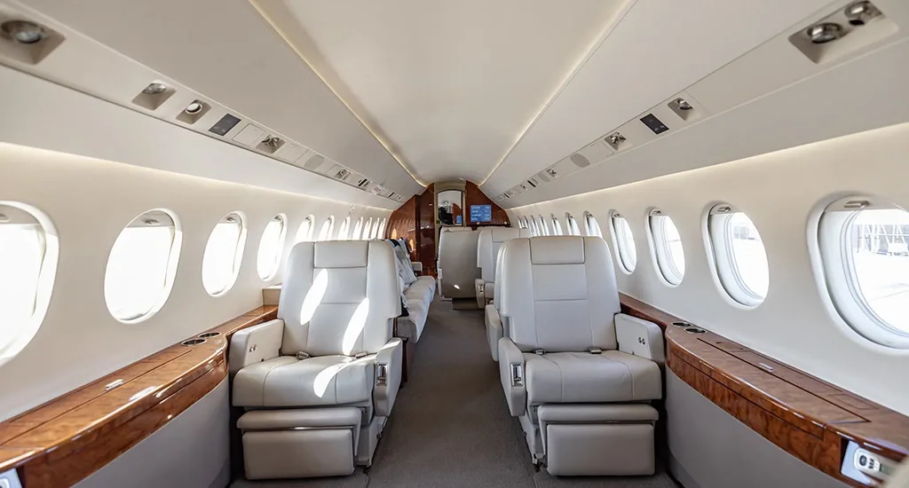 The luxurious cabin interior of a business jet, featuring light-colored leather seats and wood accents.