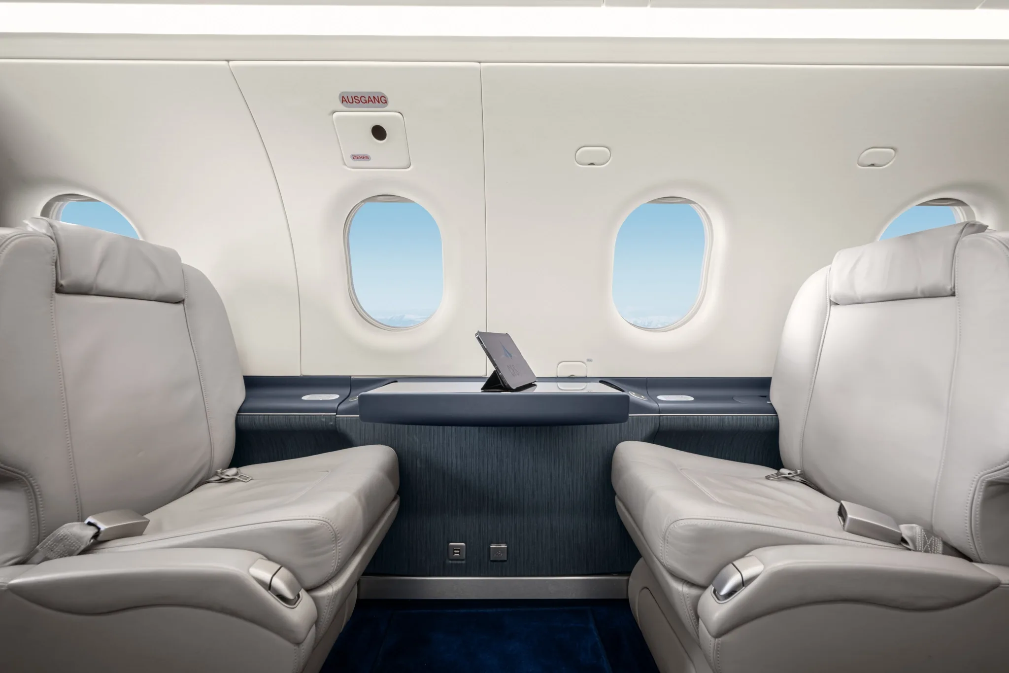 Two light grey leather seats face each other in the aircraft cabin, separated by a table with a tablet.
