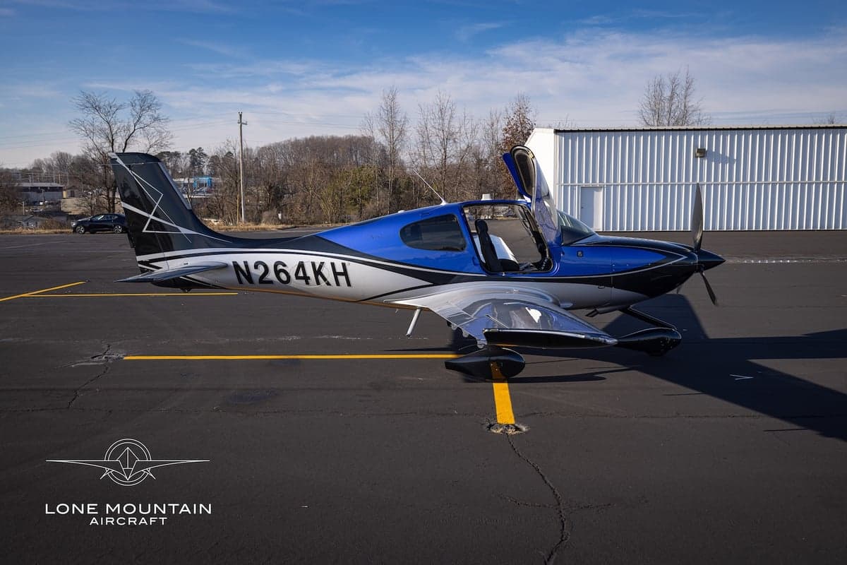 Side view of the Cirrus SR22T aircraft with registration N264KH parked on the tarmac with the doors open.