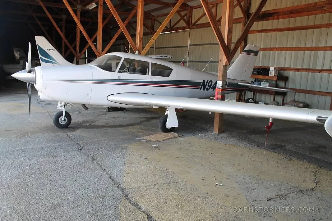 A white single-engine propeller aircraft with blue and red stripes, registration N949P, viewed from the side in a hangar.