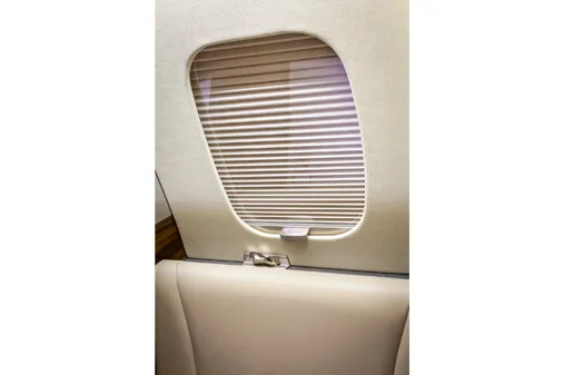 A close-up of an aircraft cabin window with closed horizontal blinds and a cream-colored seat back.