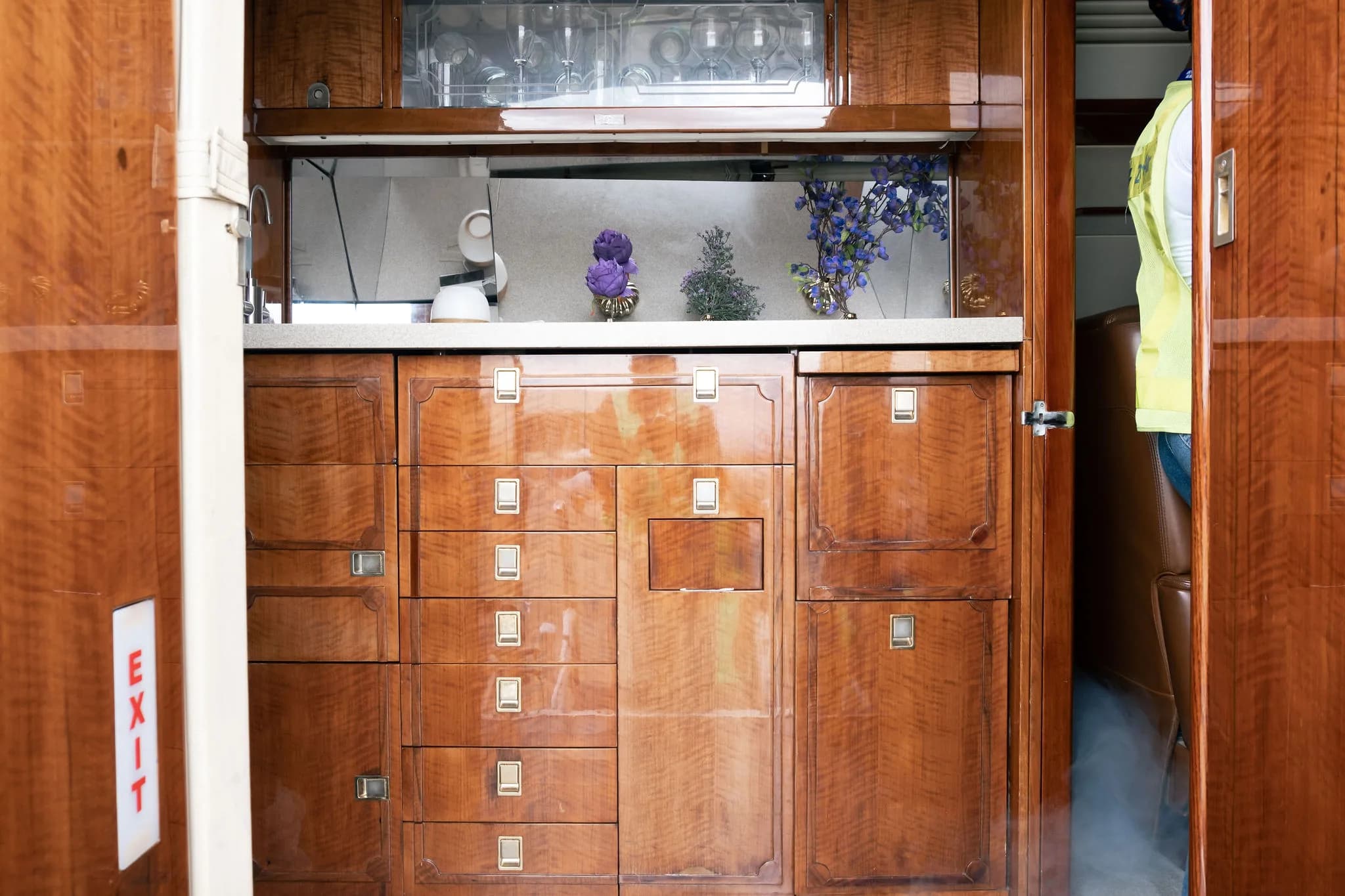 A private jet galley area with polished wood cabinets, drawers, and a counter with decorative items.