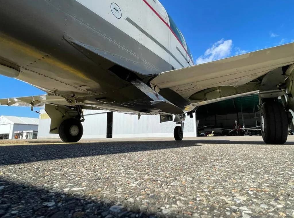 A low-angle view of the undercarriage and main landing gear of a white and red aircraft on an airfield.