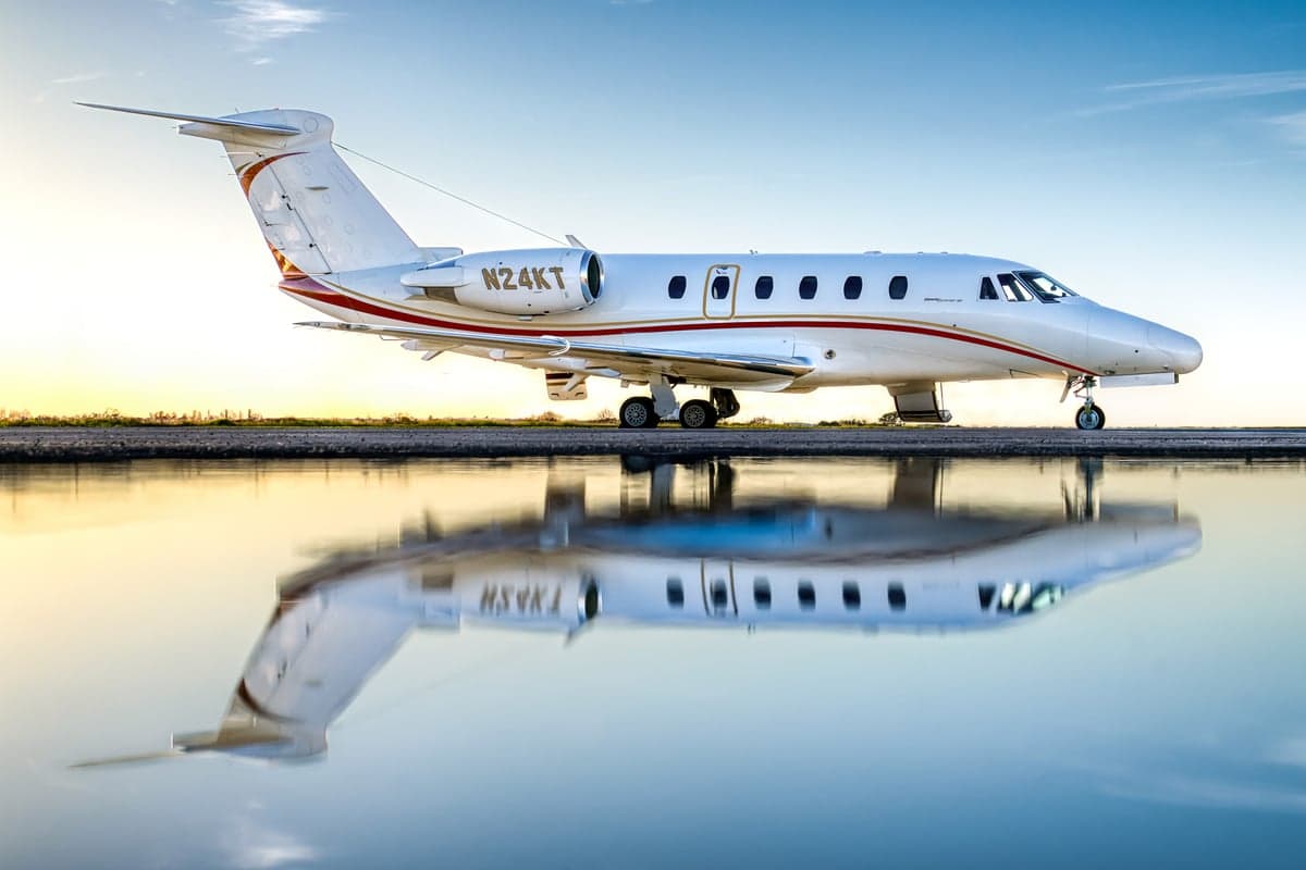 A white and red Cessna Citation is reflected in a pool of water on the tarmac.