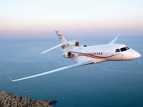 A white Falcon jet with red stripes flying over the ocean.