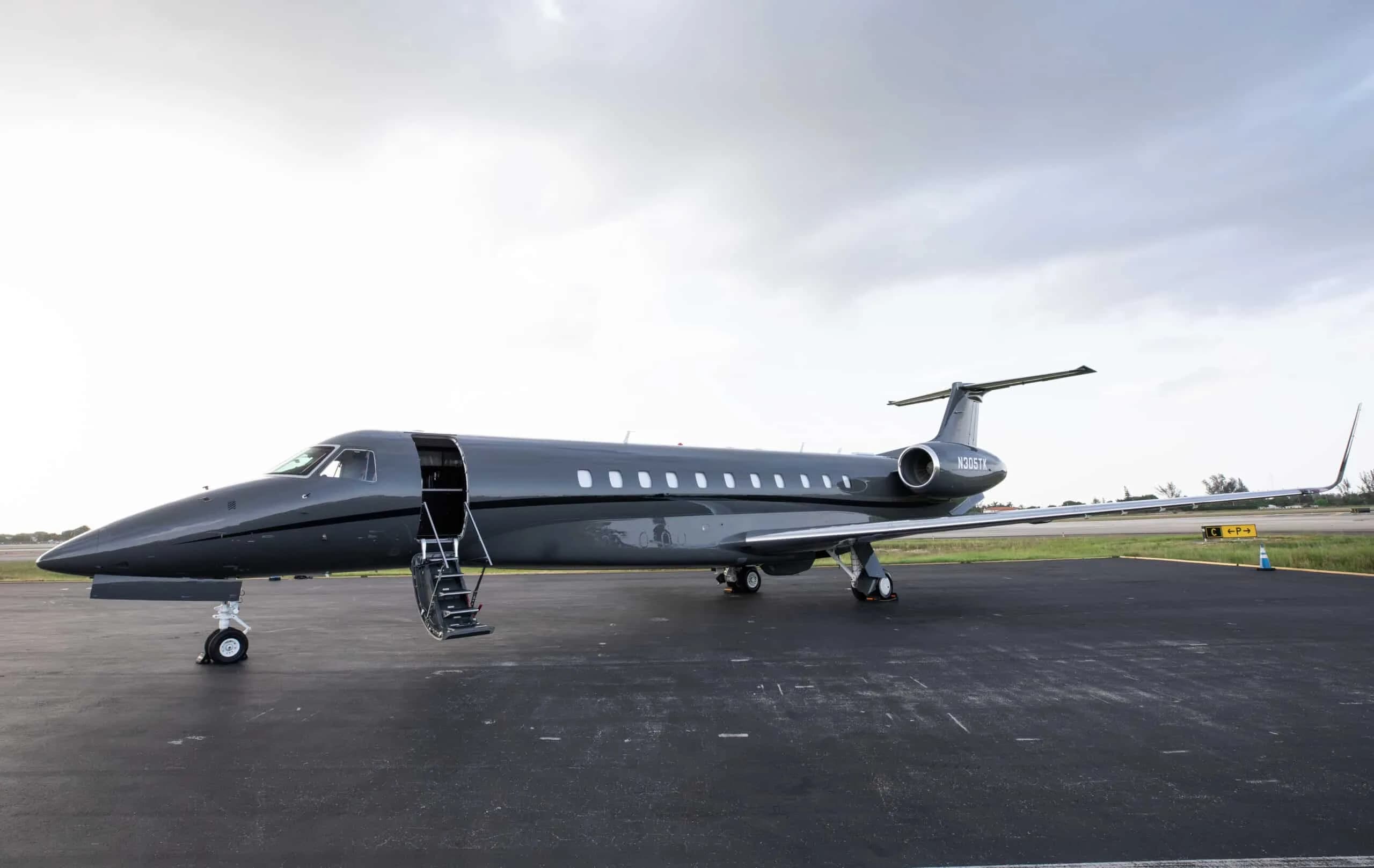 A dark grey Embraer Legacy 500 business jet, registration N305TK, parked on a tarmac with its main door open.