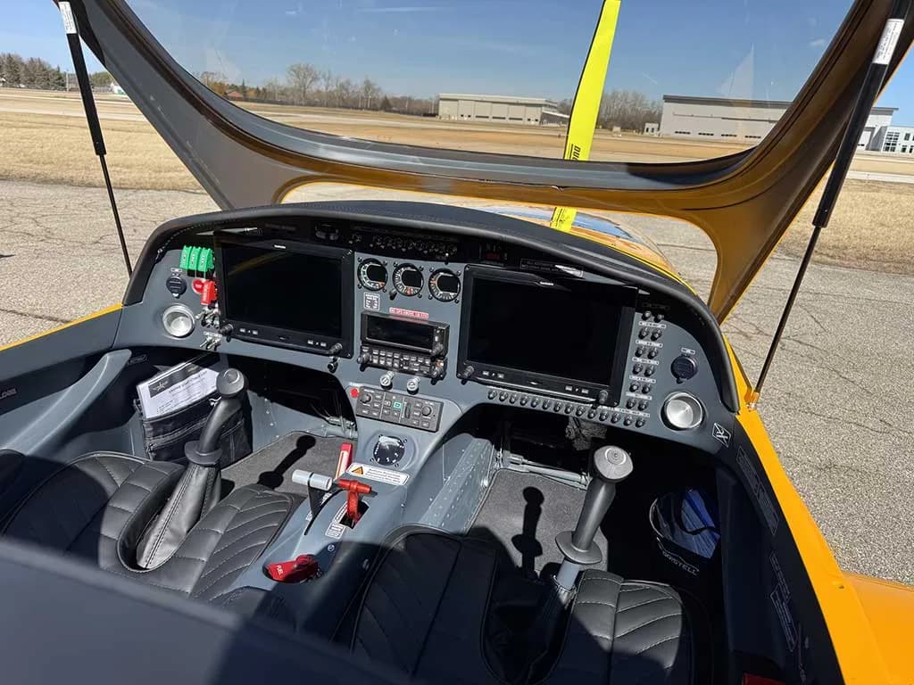 A close-up view of the Bristell aircraft's cockpit, featuring a modern instrument panel with dual displays and black quilted seats.