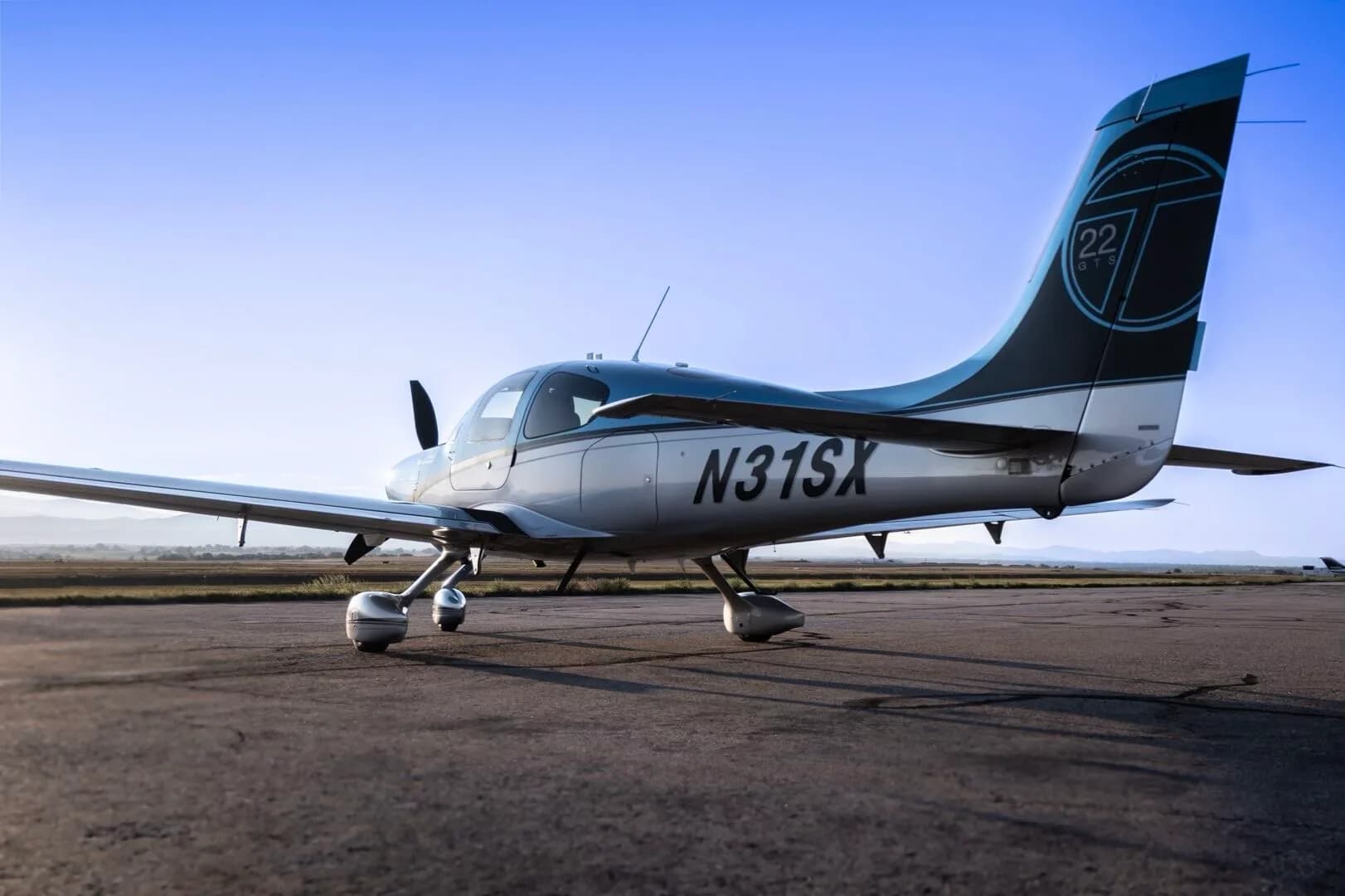 A Cirrus SR22T aircraft, N31SX, in blue and silver paint, parked on an airfield from a rear-side angle.