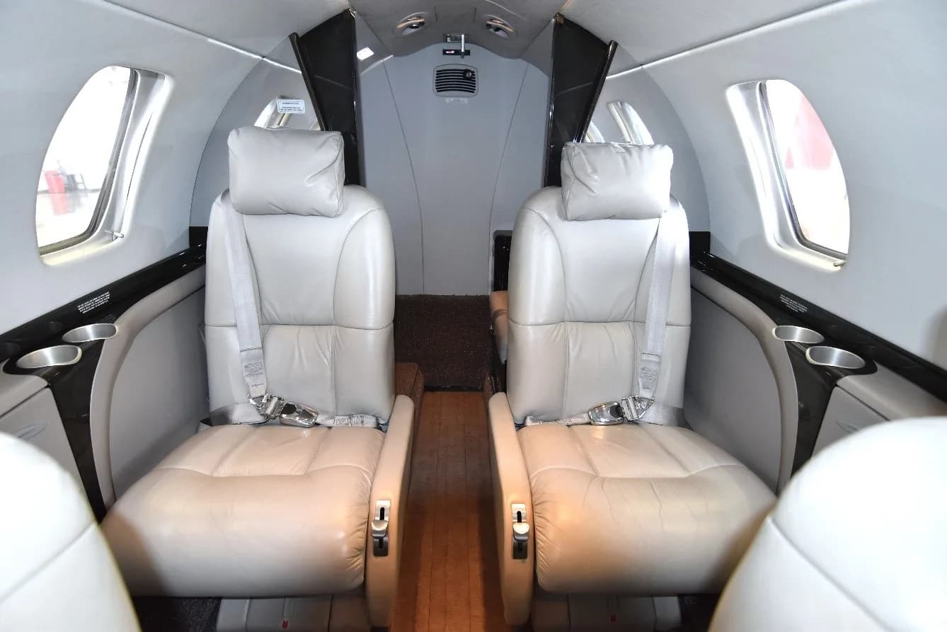 Two light gray leather passenger seats with seatbelts in the cabin of a private jet.