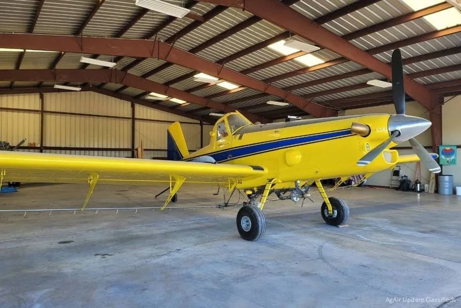 Yellow and blue crop duster aircraft in a hangar.