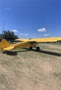 A yellow Cubcrafters aircraft is parked on the grass.