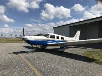 A Piper PA-28-181 Archer II aircraft with a blue and white paint scheme parked on the tarmac.