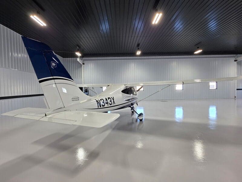 A white and blue Tecnam P2008 Light Sport aircraft (N343X) is parked in a hangar, viewed from the rear-right.