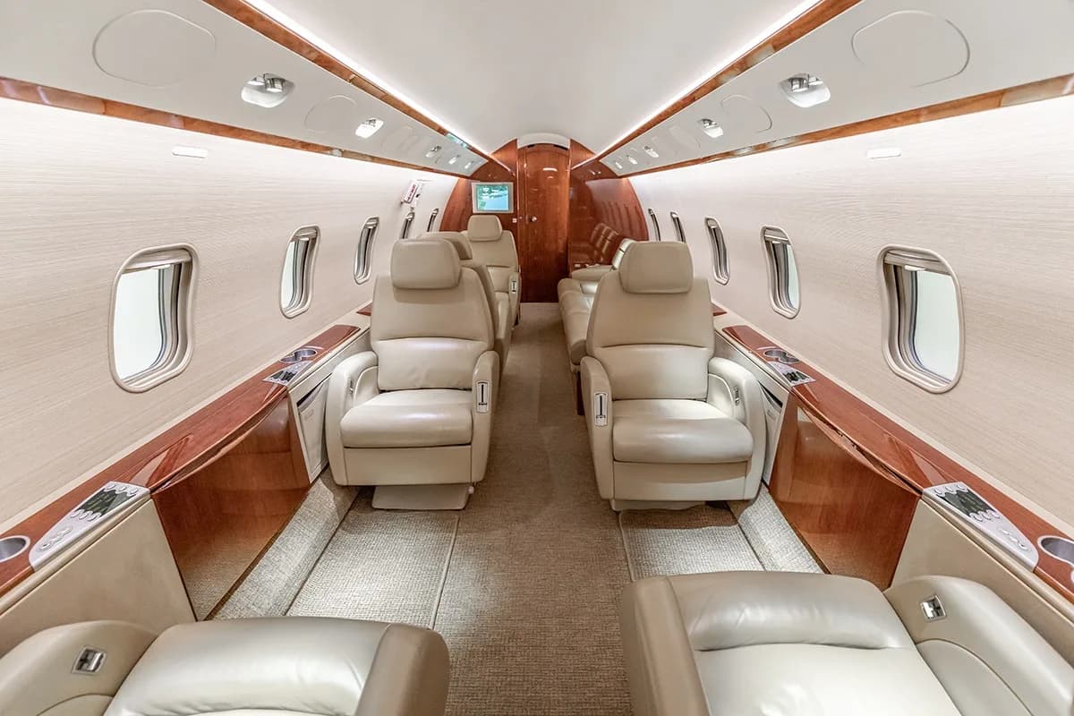 A view of the Challenger 350 cabin with beige leather seats and wood trim.