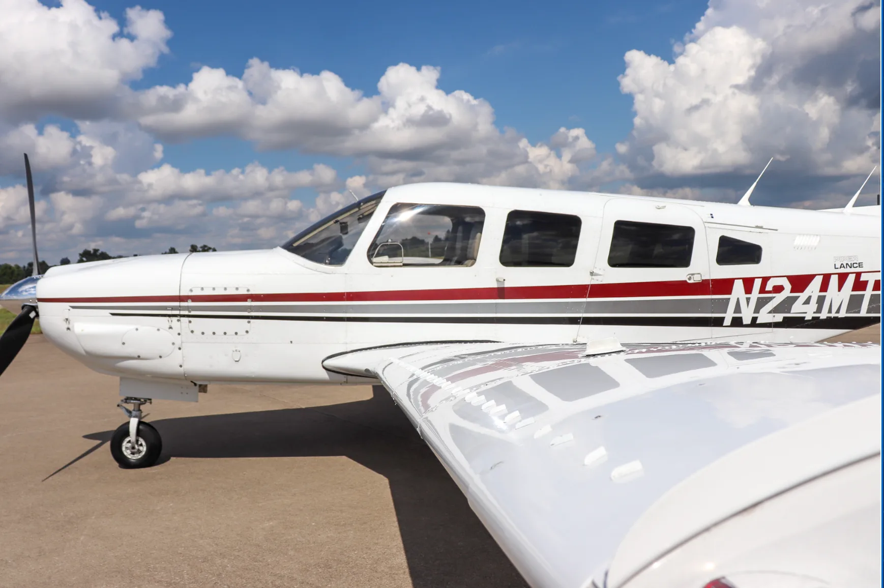 A side view of the cockpit and wing of the white Piper Lance (N24MT) with red and grey stripes.