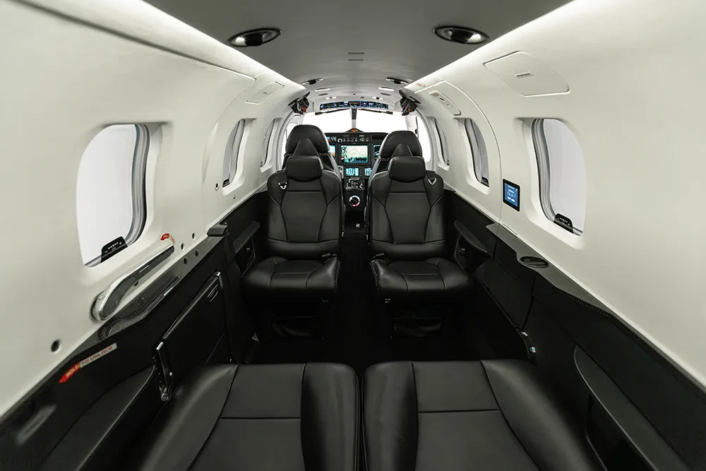 A private jet cabin with black leather seats, looking forward into the cockpit area.