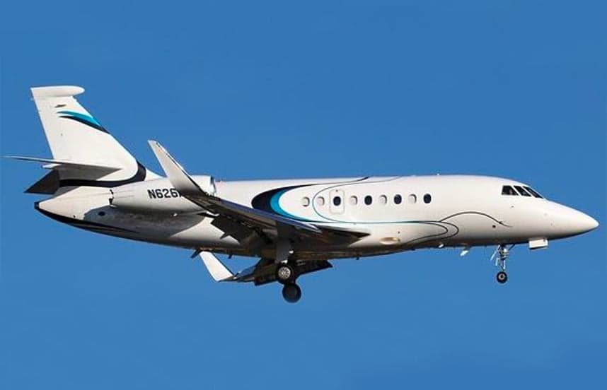 A white Falcon 2000 aircraft with blue accents is in flight against a blue sky.