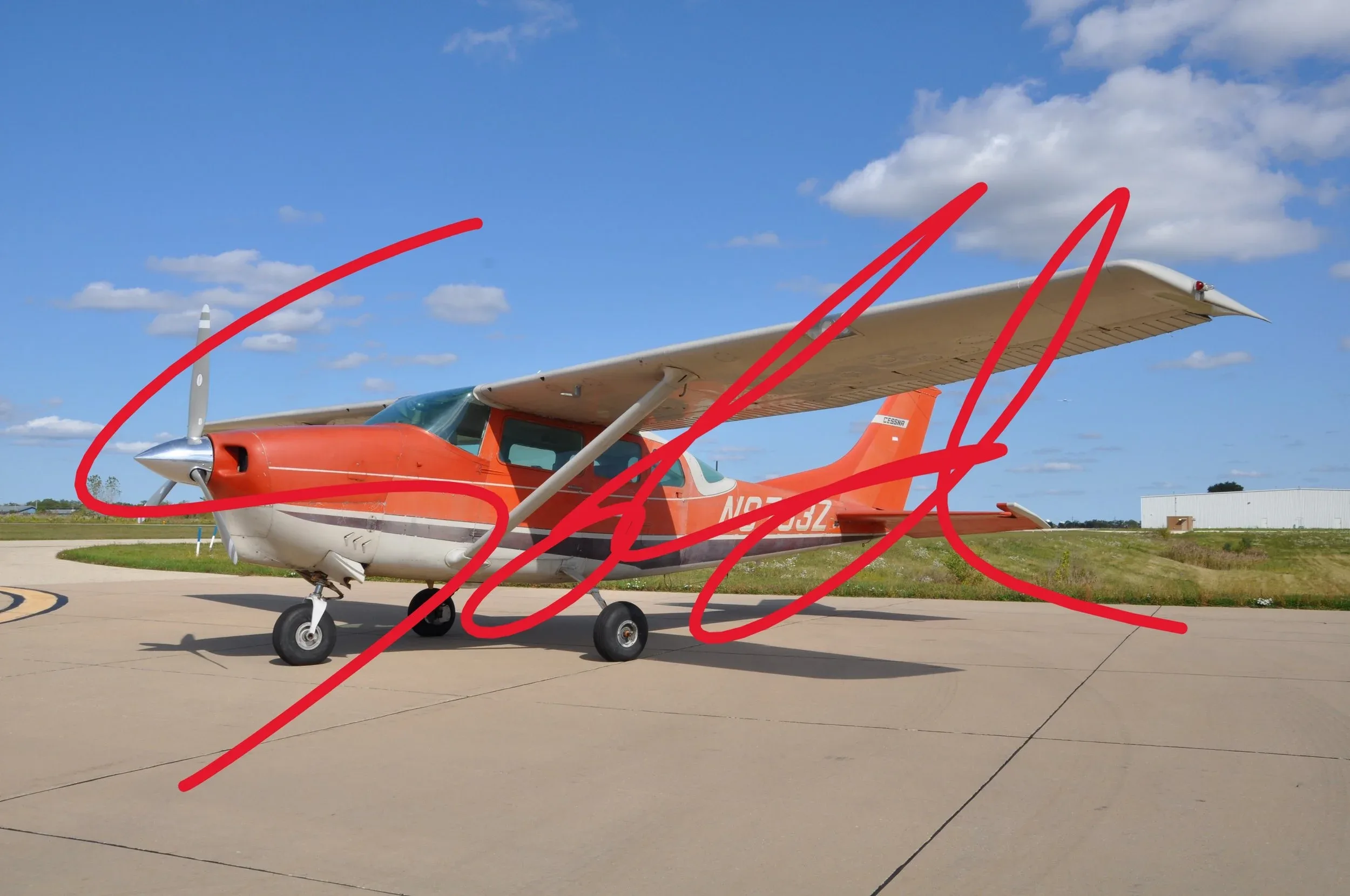 An orange and white Cessna 182 aircraft is parked on an airport tarmac under a blue sky.