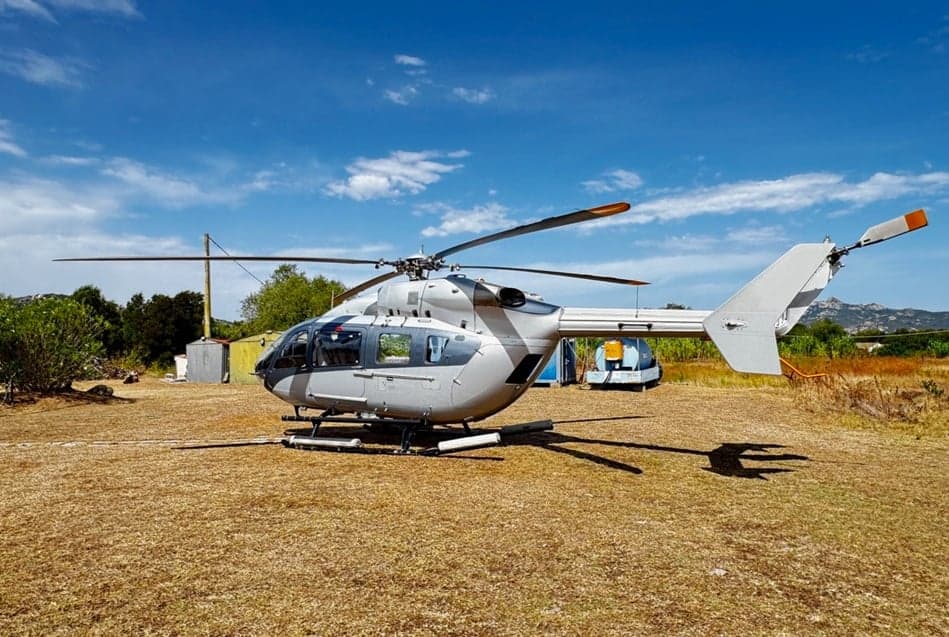 Helicopter parked on a grassy field on a sunny day.