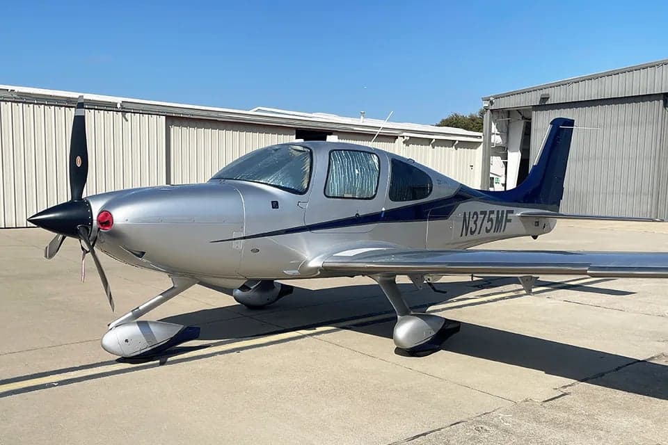 A Cirrus SR22T aircraft is parked on the tarmac with a silver and blue paint scheme.