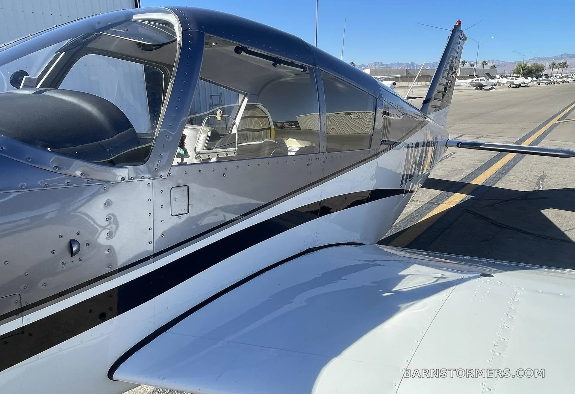 A close-up side view of the fuselage and wing of a dark gray and white Piper Cherokee 140, showing the cabin interior.