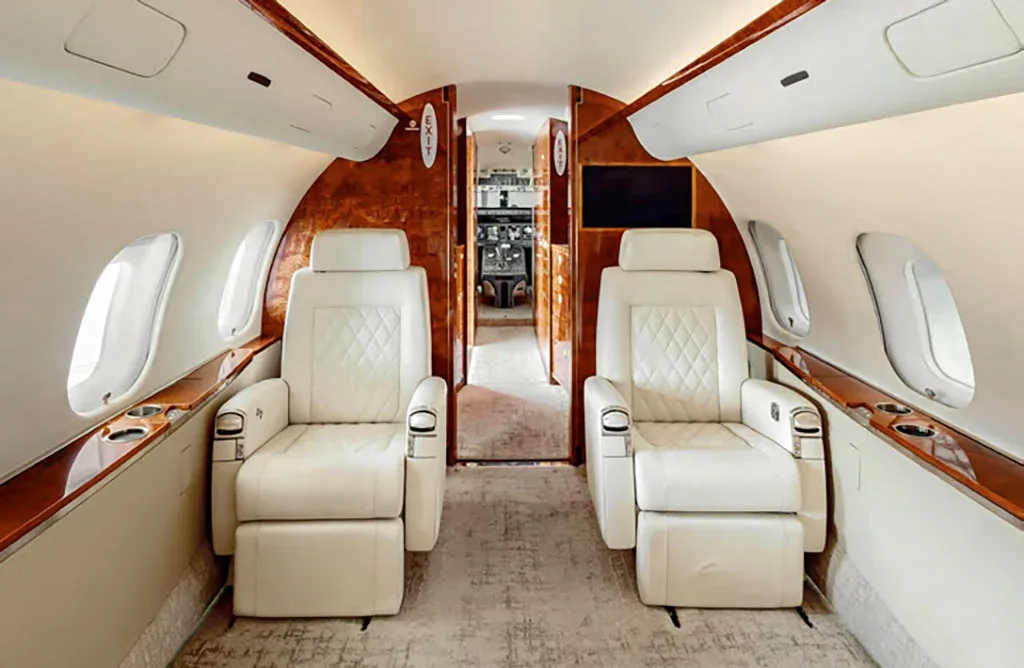 Two white quilted leather seats in the private jet cabin face forward towards the cockpit entrance.