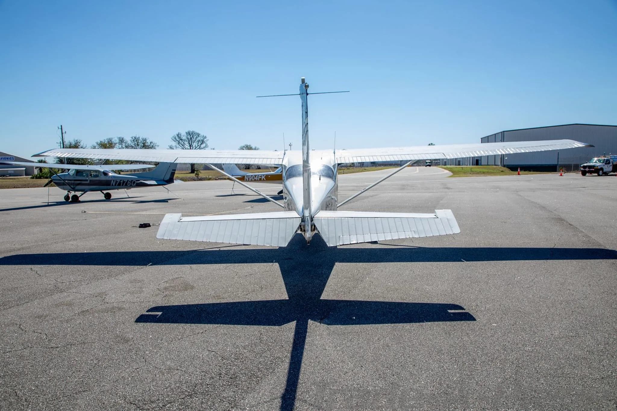 A rear view of the N86ER aircraft, a white Cessna 172, parked on an airfield with its shadow stretching forward.