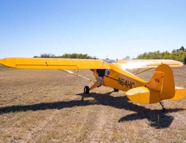 A side view of the yellow Legend Cub aircraft, registration N64HC, parked on a grassy field under a clear sky.