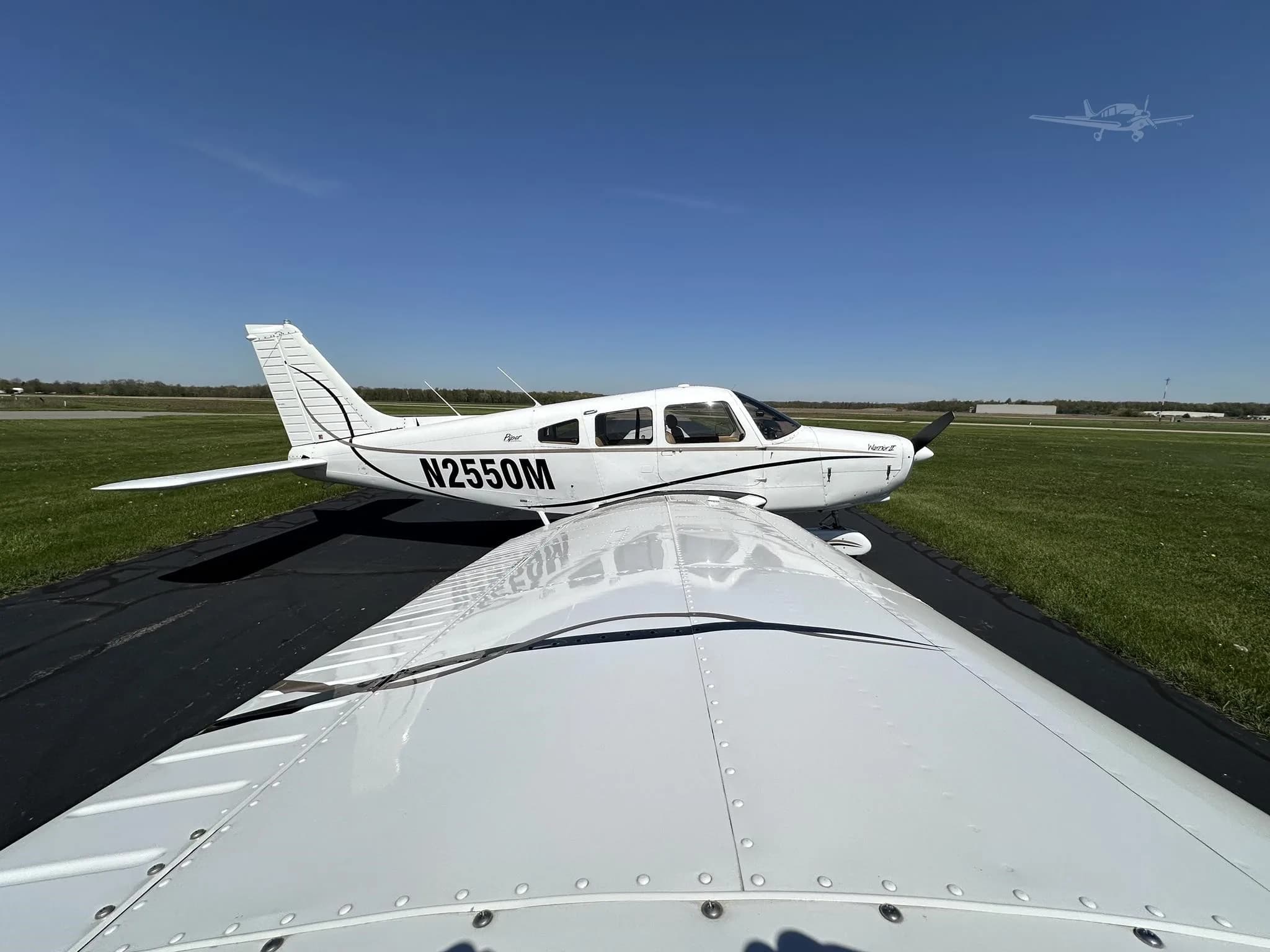 A view looking over the white wing of a Piper Cherokee towards the fuselage of the aircraft N2550M on a runway.