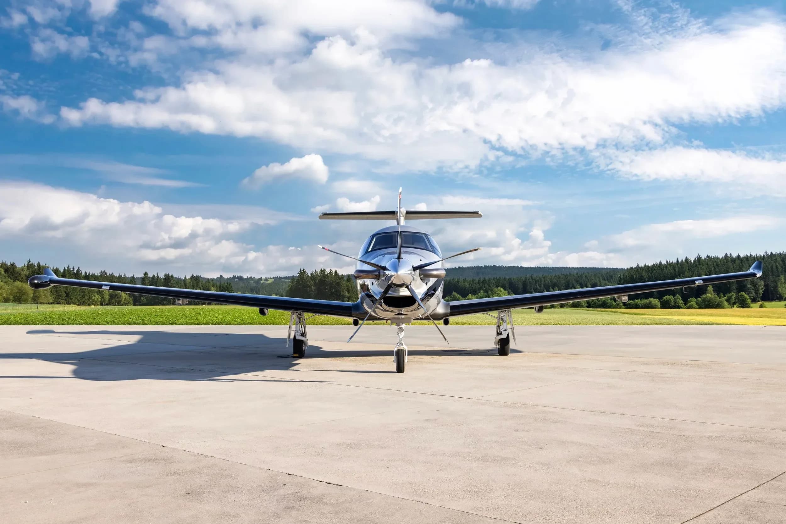 A head-on view of a silver Pilatus PC-12 NG aircraft with a black propeller, parked on a tarmac.
