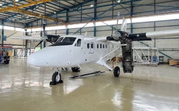 A white twin-engine turboprop aircraft with an open engine cowling sits inside a hangar.