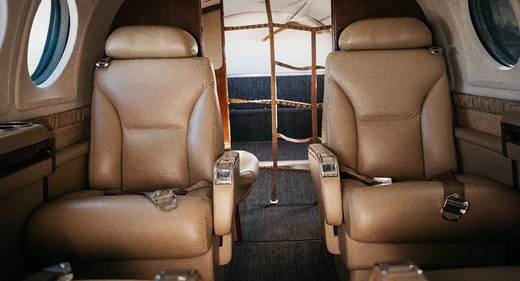 Two tan leather passenger seats in the aircraft cabin, facing forward.