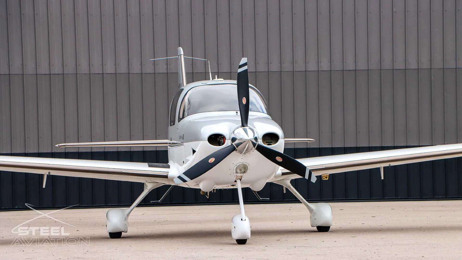 A close-up front view of the white and silver Cirrus SR22 aircraft, showing the propeller and nose.