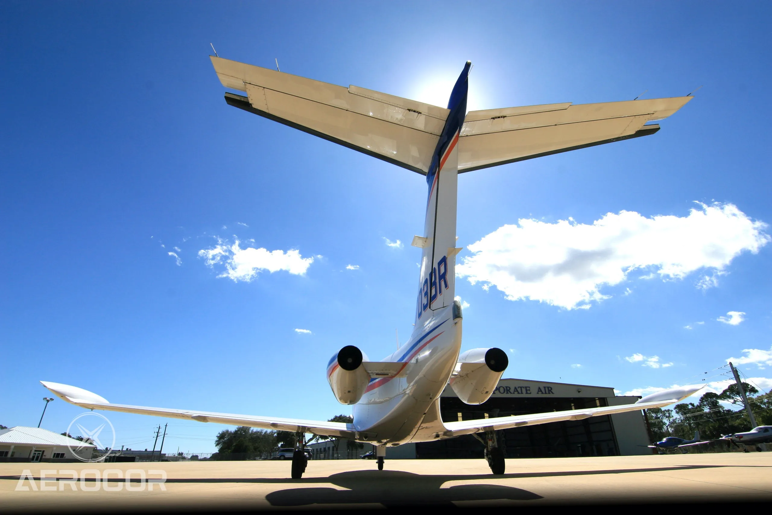 A rear view of a white Eclipse 500 jet with blue and orange stripes, tail number N703BR, showing its V-tail and engines on an airfield.