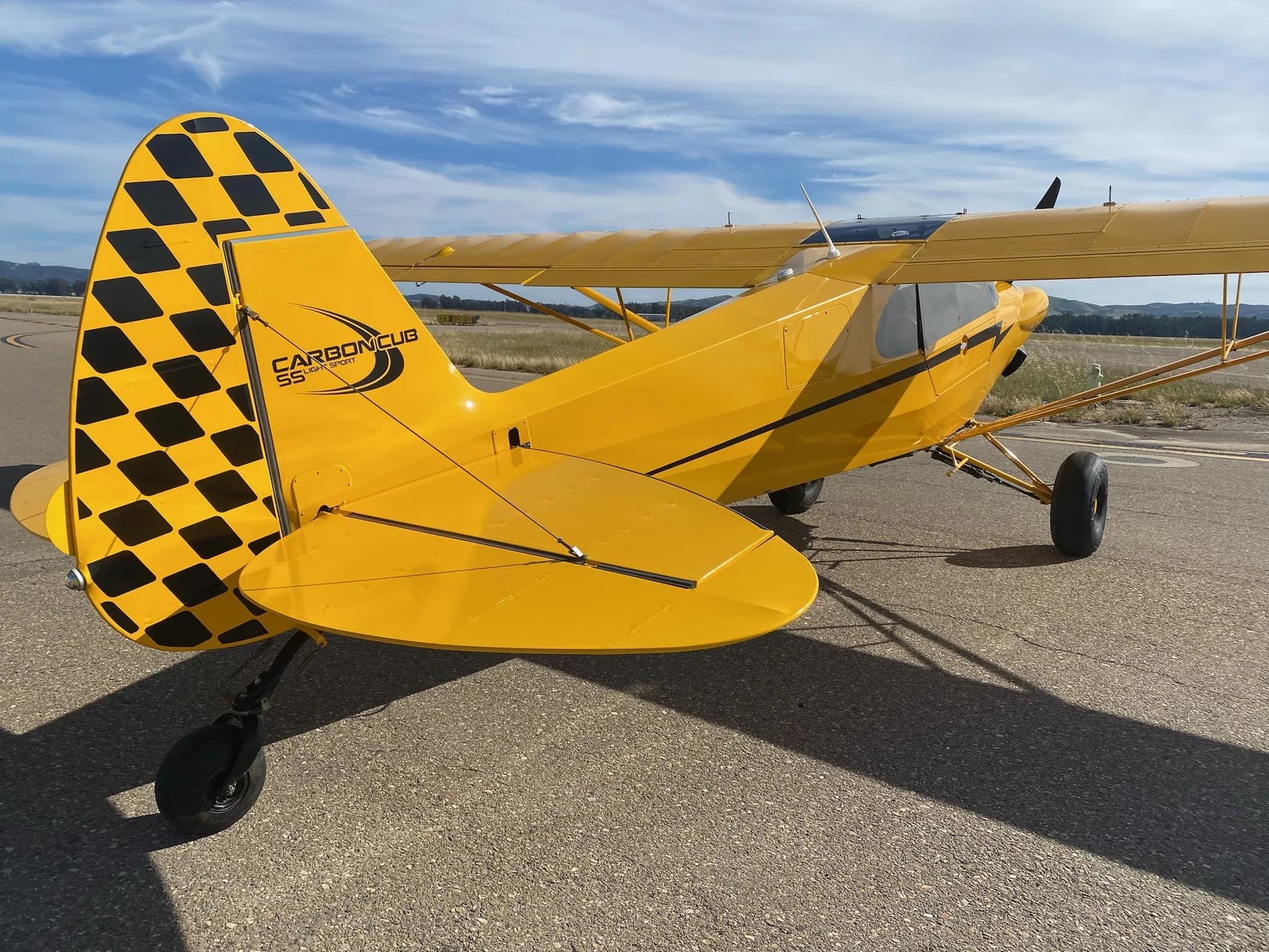 A yellow Carbon Cub aircraft with a checkered tail is parked on the tarmac.