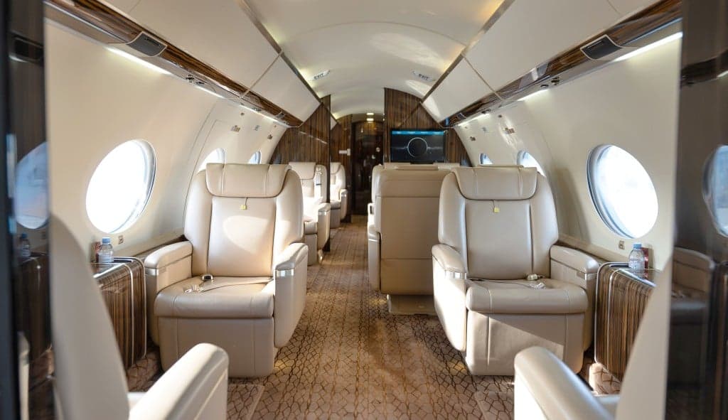 A white and gold Gulfstream jet is parked on the tarmac in front of a hangar.