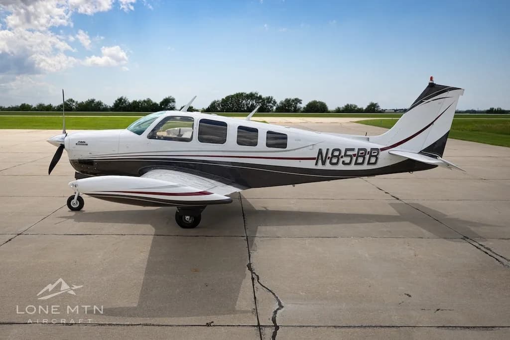 A side view of a white and dark grey Beechcraft Baron N85BB parked on a tarmac.
