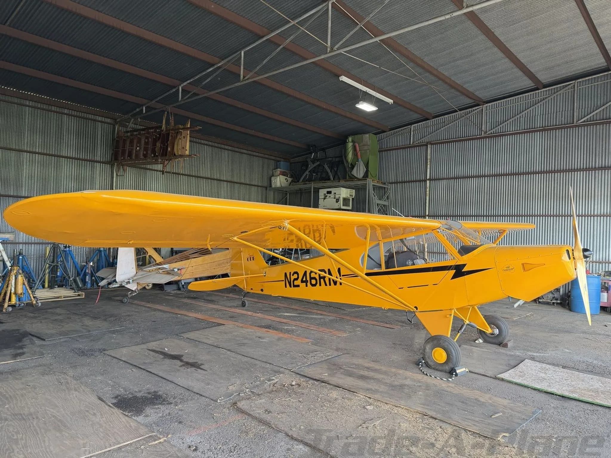 Side view of a yellow American Legend Cub aircraft with registration N246RM parked in a hangar.