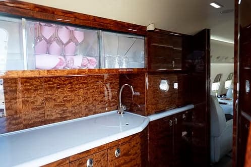 A close-up of the private jet's galley area with a sink, polished wood cabinetry, and glassware storage.