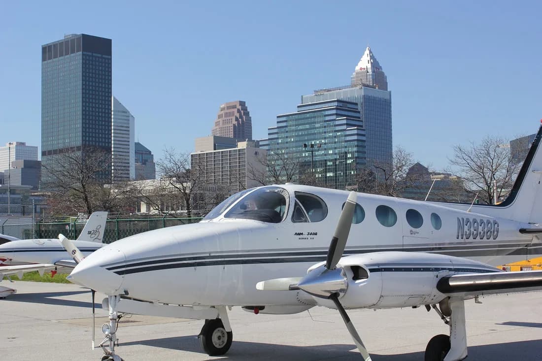 A white and gray Piper PA-31T Cheyenne II aircraft parked in front of a city skyline.