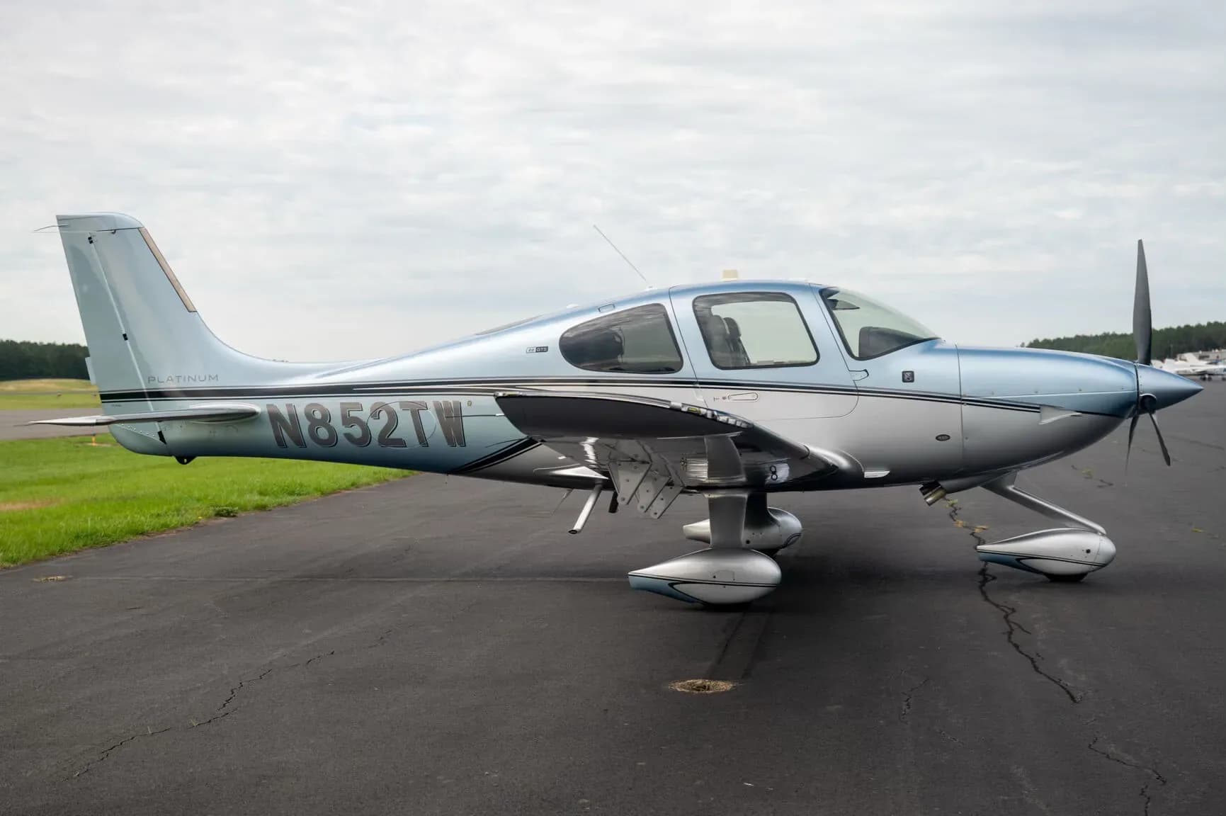 A side view of a blue and silver Cirrus SR22 aircraft, N852TW, parked on an asphalt tarmac.